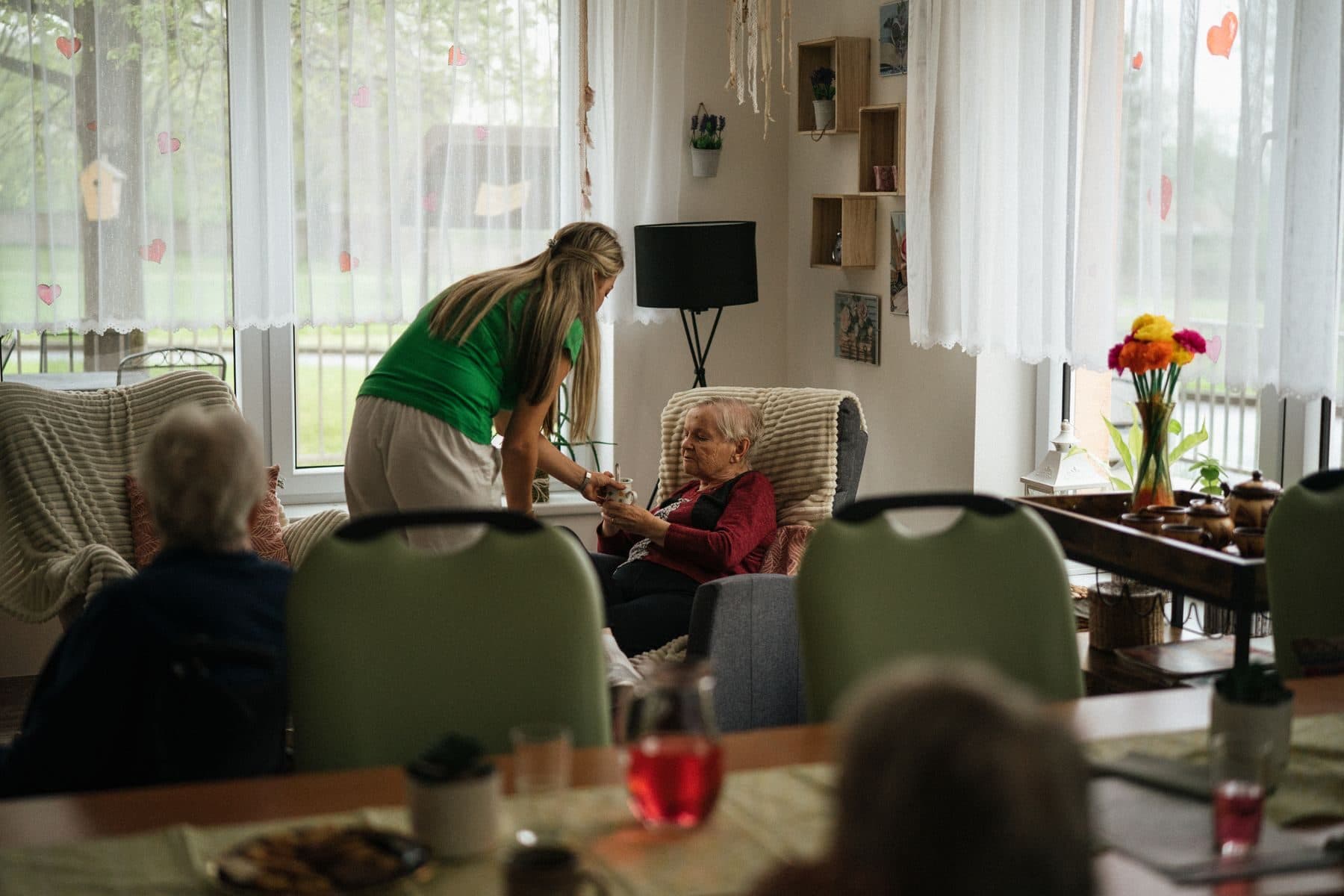 A carer handing a warm drink to an older woman in an armchair